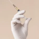 Gloved hand holding syringe with liquid injection on neutral background